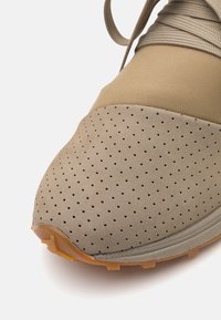 Beige sportieve schoen met geperforeerde textuur, glad bovenwerk en rubberen zool. Beschikt over tonale veters en een gevoerde enkel voor extra comfort.