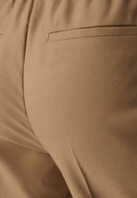 Nahaufnahme von beigen Stoffhosen, die die Gesäßtasche und Nahtdetails zeigen.