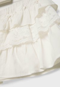 Hvidt stof med rynkede flæser og detaljer i blomsterblonde, der viser lagdelt struktur og blødt materiale.