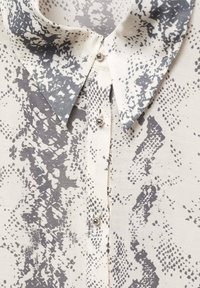 Hemd mit Knopfleiste aus leichtem Stoff mit einem grauen und weißen abstrakten Muster. Auffällige Details sind der spitze Kragen und glänzende Knöpfe.
