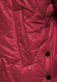 Rode gewatteerde jas met een soepele textuur, drukknoopsluiting en een kenmerkend logotag, met een slanke zakdetail aan de voorkant.