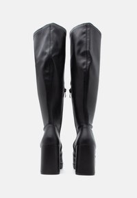 Bottes noires montantes en cuir, dotées d'un talon carré, d'une fermeture éclair latérale et d'une finition lisse avec des détails de couture discrets.