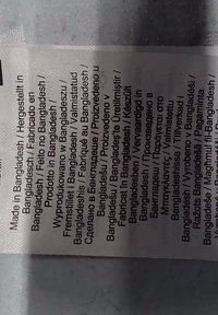 Étiquette de soins pour lessive avec texte noir sur un fond de tissu blanc, affichant des informations multilingues sur la fabrication au Bangladesh.