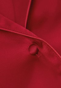 Czerwony materiał o gładkiej teksturze, z zaokrąglonym guzikiem i złożonymi brzegami, pokazujący elegancki i dopasowany design.