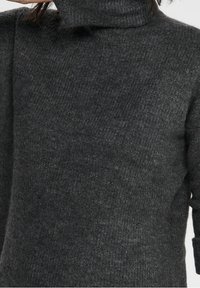 Pull à col roulé en tricot épais gris foncé avec une finition texturée ; design ample et manches longues.