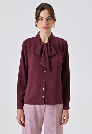 Burgundy blouse with a bow tie collar, long sleeves, button front, and glossy buttons. Made from smooth fabric with a draped fit.