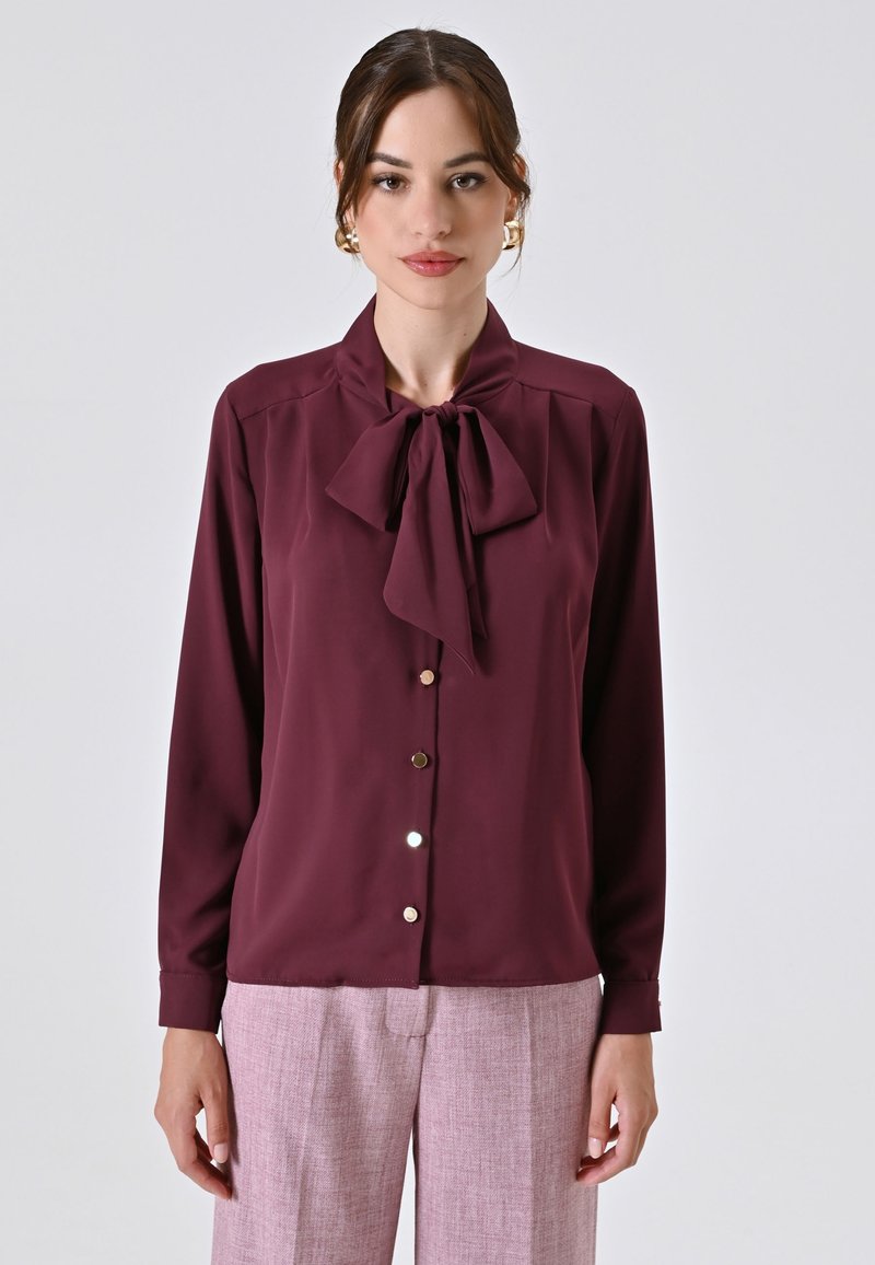 Burgunderfarbene Bluse mit einerm Schlipskragen, langen Ärmeln, Knopfverschluss und glänzenden Knöpfen. Hergestellt aus glattem Stoff mit eleganter Passform.