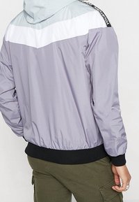 Lättviktsjacka i färgblock med paneler i lavendel, vitt och ljusblått, med elastiska ärmslut och huva, tillverkad av slätt nylonmaterial.
