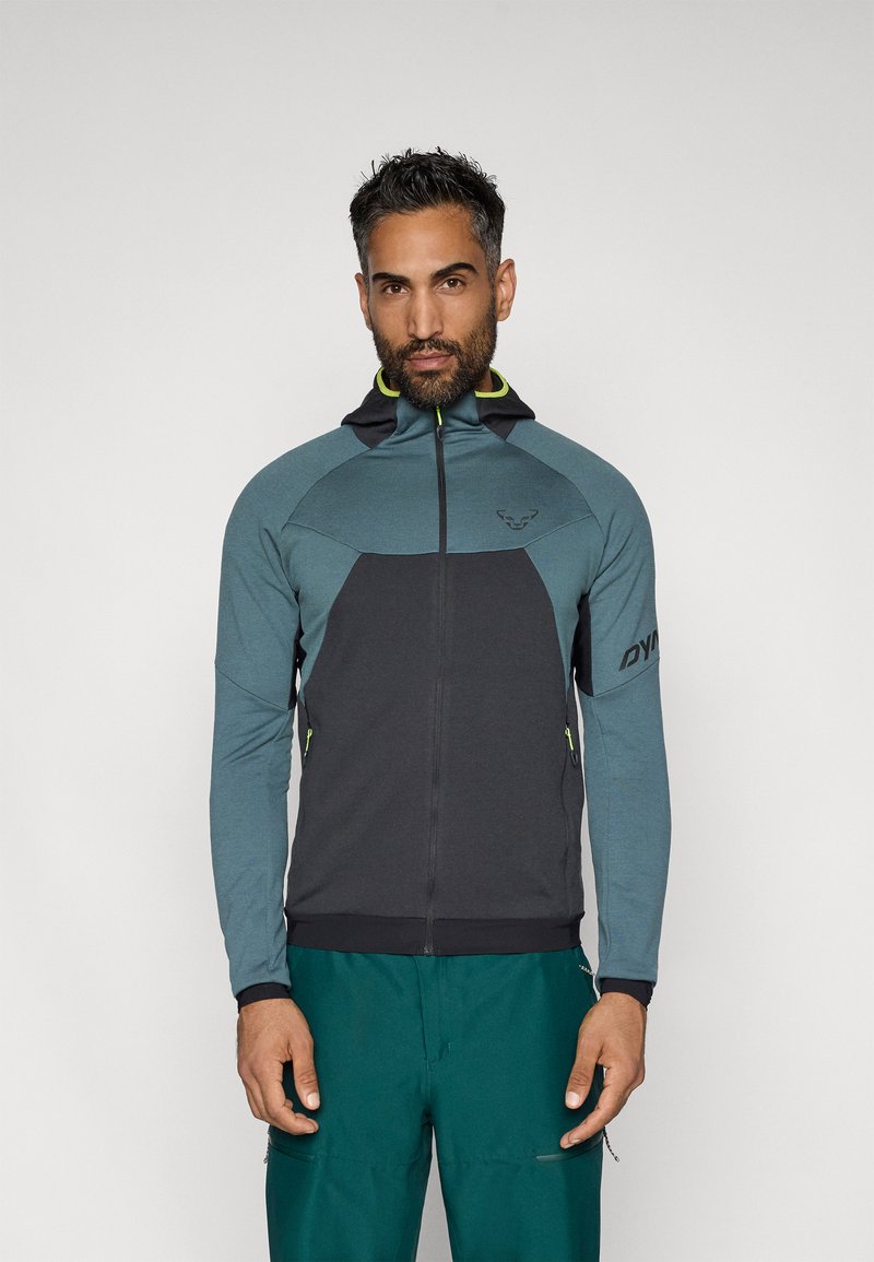Kapucnis, sötétszürke és türkiz anyagú, kontrasztos sárga részletekkel ellátott zipzáras dzseki, oldalsó zsebekkel és ergonómikus kialakítással.