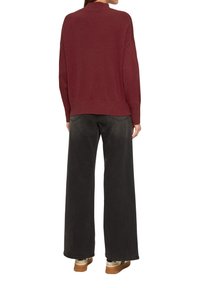 Bordeaux gebreide trui met hoge hals, gecombineerd met brede zwarte broek en lichtgekleurde sneakers met accenten.