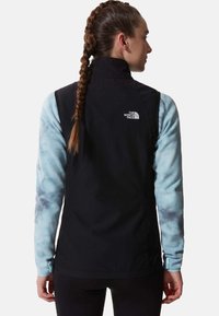Schwarze Zip-Weste mit hohem Kragen, kombiniert mit langen Ärmeln im blauen Batikmuster, auf der Rückseite mit dem North Face-Logo.