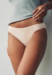 Bežna bombažna hlačica z ženskem pridihom v obliki pentlje, brezšivne robove in lahkotno, gladko teksturo. Nošena pod sivo rebrasto majico.