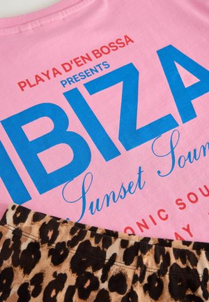 Tricou roz din bumbac, cu text albastru și roșu care spune "Ibiza Sunset Sounds". Un model cu imprimeu leopard în partea de jos adaugă contrast.