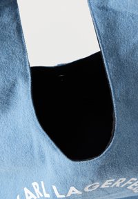 Saco de lona de denim azul com uma grande abertura superior, apresentando uma superfície texturizada e interior preto. Logótipo branco impresso na frente.