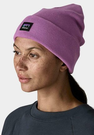 Gorro de punto acanalado morado con un parche negro de Patagonia. El modelo lleva una sudadera oscura, lo que resalta la forma y textura únicas del gorro.