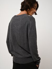 Harmaa neulottu neuletakki rennolla leikkauksella, pyöreällä kaula-aukolla ja ribbauslahkeilla. Pehmeä rakenne, jossa on minimaalista yksityiskohtaisuutta, kuvattu takaa.