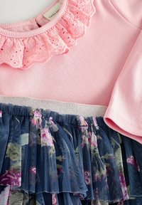 Rosa Baumwolltop mit einem Spitzenvolant am Ausschnitt, kombiniert mit einem marineblauen floralen Netzrock mit einem silberakzentuierten Taillenbund.