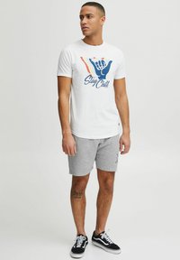 Hvid bomulds T-shirt med et farverigt håndgrafik og teksten "Stay Chill". Båret med grå shorts og sorte sneakers.