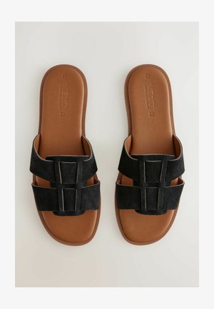 Sandales à glissière en suède noir avec un design à double bande, présentant une semelle marron lisse et une construction minimaliste pour le confort.