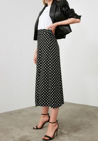 Falda midi negra con lunares, de cintura alta, combinada con una camiseta blanca y una americana negra. Presenta sandalias de tacón alto negras con tiras.