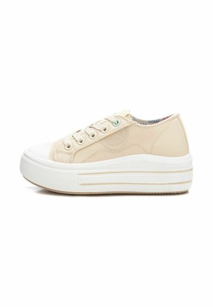 Zapatilla de lona beige con punta redondeada, suela de goma blanca y parte superior texturizada. Presenta un cierre de cordones en la parte delantera y sutiles acentos decorativos.