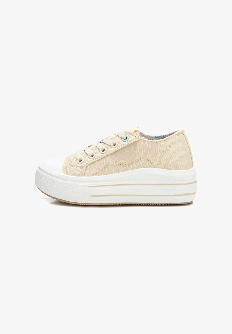 Zapatilla de lona beige con punta redondeada, suela de goma blanca y parte superior texturizada. Presenta un cierre de cordones en la parte delantera y sutiles acentos decorativos.
