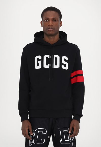 Hoodie noir avec logo "GCDS" blanc, rayures rouges sur les manches, capuche avec cordon de serrage, tissu doux, coupe décontractée. Porté avec un short noir.