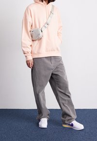 Ljusrosa sweatshirt med huva, grå kordfl/database byxor och vita sneakers med lila och gula detaljer. Inkluderar en grå axelväska.