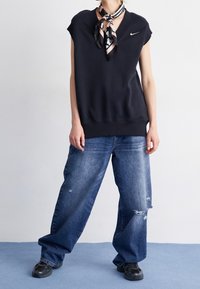 Mörk kortärmad sweatshirt med V-ringning och litet logotyp, ihopparad med slitna vid jeans i blått och svarta sportskor. Silkscarf knuten runt halsen.