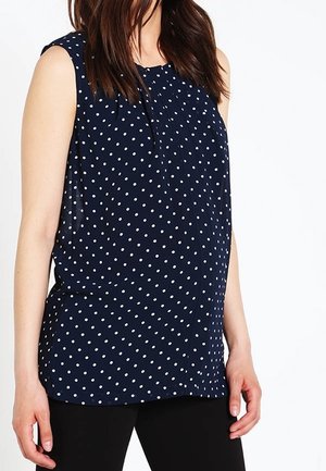 Granatowy top bez rękawów w białe kropki, z okrągłym dekoltem i miękkim układem. Noszony z czarnymi dopasowanymi spodniami.