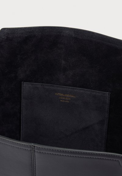 Μαύρο βελούδινο εσωτερικό μιας τσάντας με ραμμένη τσέπη που φέρει χρυσά γράμματα: "Victoria Beckham N°202VB099 Κατασκευάστηκε στην Ιταλία."