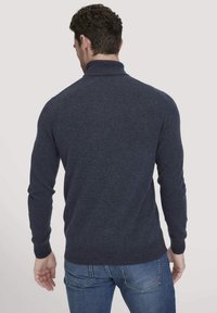 Marineblauer, langärmliger Pullover aus einem weichen Strickstoff, mit einem hohen Kragen und gerippten Bündchen, getragen mit blauen Jeans.