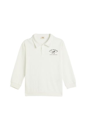 Valkoinen pitkähihaine polo-paita, ribsikangas, jossa on musta printti "Lucky Wildlife" ja lehmäkuva rinnassa.