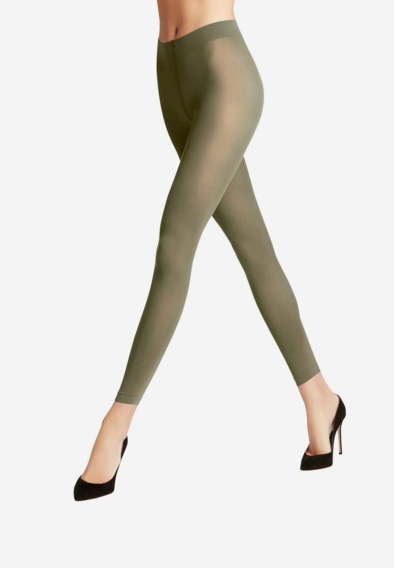Olivengrüne Leggings aus einem transparenten Material, mit einem hohen Taillenbund und glatter Textur, kombiniert mit schwarzen hohen Absätzen.