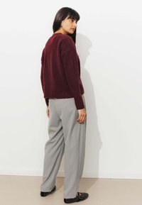 Pull bourgogne à coupe décontractée, associé à un pantalon gris clair à rayures. Texture douce, col rond et chaussures noires plates avec des clous.