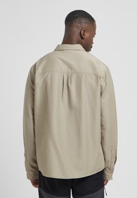 Beige overhemd met lange mouwen en een ontspannen pasvorm, met knoopmanchetten en een rugplooi, gemaakt van een soepele, lichte stof.