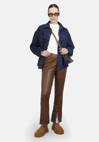 Denim jack, witte trui, bruine faux leren broek met splits, bruine schoenen en oranje rechthoekige zonnebril. Zwarte schoudertas.