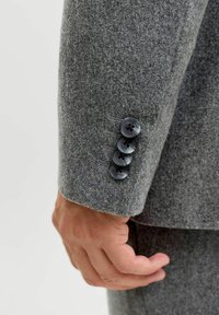 Halli villa bleiseri varrukas, millel on neli tumedat nuppu ja peen õmblusdetail. Kangal on pehme tekstuur ja minimaalne muster.