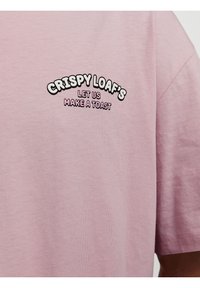 Pink bomulds t-shirt med sort og lyserød broderet tekst: "CRISPY LOAF’S LAD OS SKÅLE." Korte ærmer og blød stofstruktur.