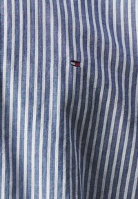 Blauw-wit gestreepte stof met een textuur. Bevat een klein geborduurd logo met rode, witte en blauwe accenten.