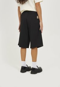 Black, knee-length shorts made of a textured material, featuring two back pockets and a small branded label on the right pocket.