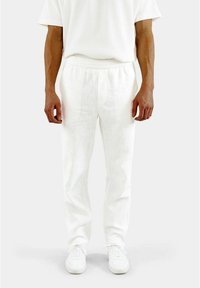 Weiße Leinenhosen mit einem elastischen Bund, schmalem Schnitt und leichtem Textur. Kombiniert mit weißen Sneakers für einen harmonischen Look.