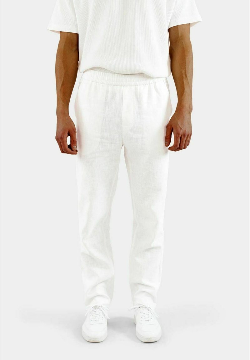 Weiße Leinenhosen mit einem elastischen Bund, schmalem Schnitt und leichtem Textur. Kombiniert mit weißen Sneakers für einen harmonischen Look.