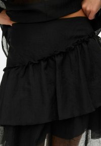 Czarna warstwowa spódnica wykonana z lekkiego materiału z falbaniastym dołem, charakteryzująca się gładką fakturą i dopasowanym pasem.