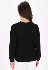 Sudadera negra de manga larga, cuello redondo y puños acanalados. Textura suave con un corte relajado. Diseño minimalista, sin patrones visibles.