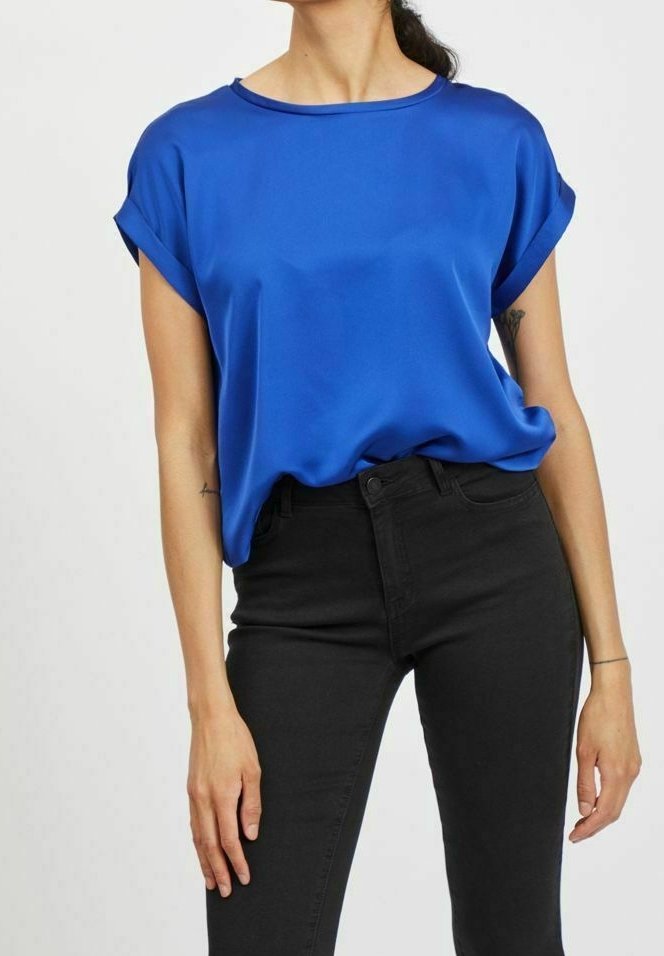 Kortärmad, rundhalsad topp i livfull blå satin, med en avslappnad passform och upprullade ärmar, kombinerad med åtsittande svarta jeans.