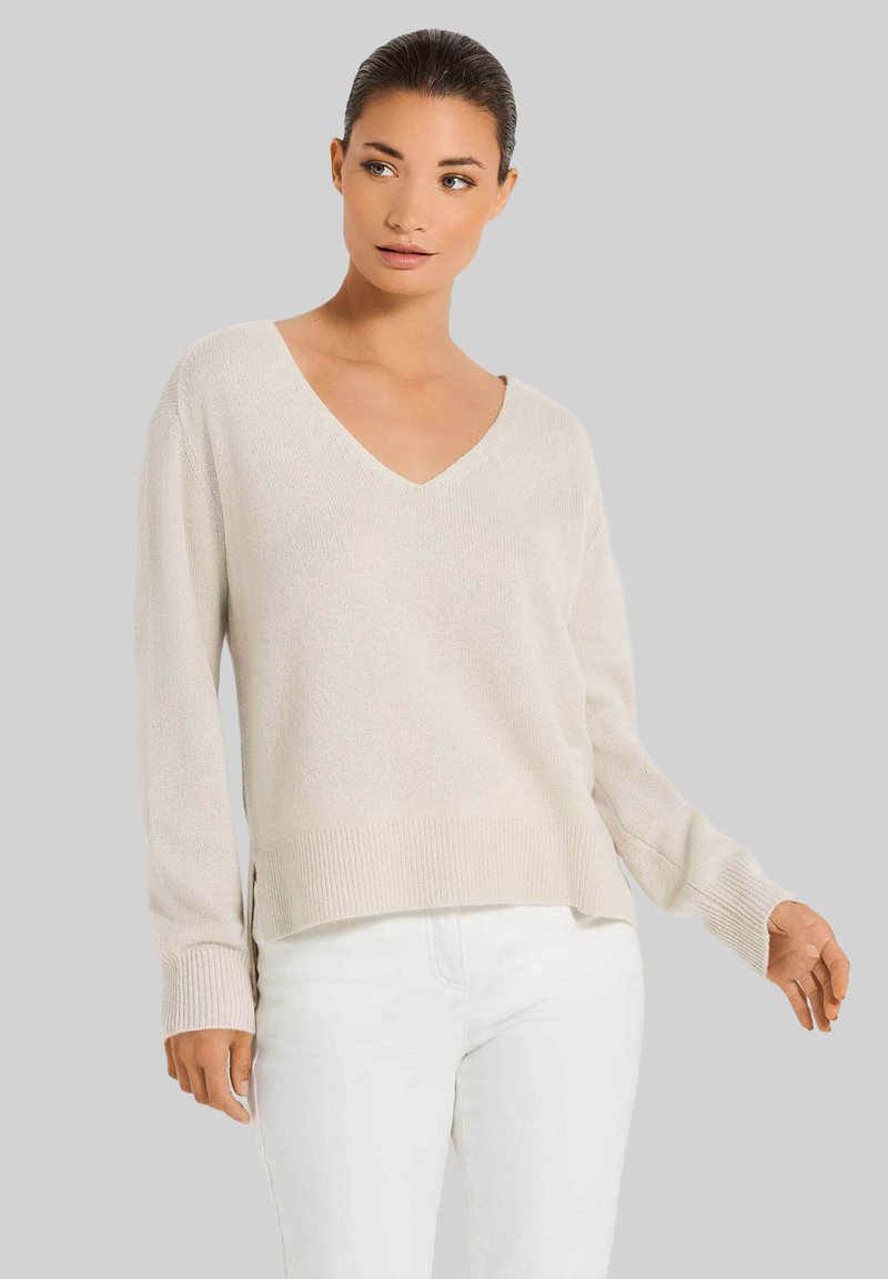 Hellbeige Strickpullover mit V-Ausschnitt, langen Ärmeln und geripptem Saum. Beinhaltet seitliche Schlitze, weiche Textur und lockere Passform.