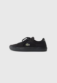 Sneaker in rete nera con punta rotonda, superficie texturizzata, suola in gomma nera e accento logo verde sul lato. Lacci davanti.
