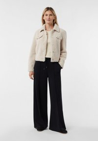 Jasnobeżowa kurtka ze sztucznego futra z dwoma kieszeniami na piersiach, zapinana na guziki, z kołnierzem. Połączona z czarnymi spodniami o szerokich nogawkach.