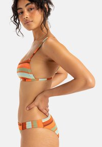 Randig bikiniuppsättning i orange, gröna och bruna nyanser. Har tunna remmar och en strukturerad tygkvalitet med ribbade mönster på båda delarna.